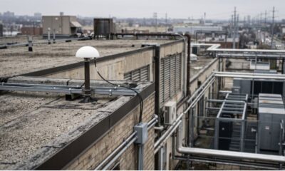 Photorealistic image of a rooftop GNSS antenna connected by cable toward an equipment room below.