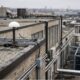 Photorealistic image of a rooftop GNSS antenna connected by cable toward an equipment room below.