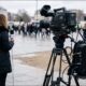 Photograph of a field reporter's backpack-mounted bonded streaming encoder with multiple cellular antennas visible, connected to a professional video camera at an outdoor news location.