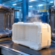 Freshly ejected white blow molded case shell resting beside an open steel mold in a plastics factory.